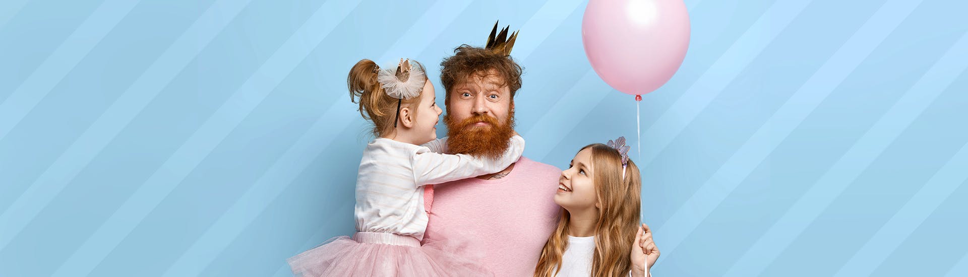 Un père de famille, entouré de ses deux filles, déguisé en princesse sur fond bleu